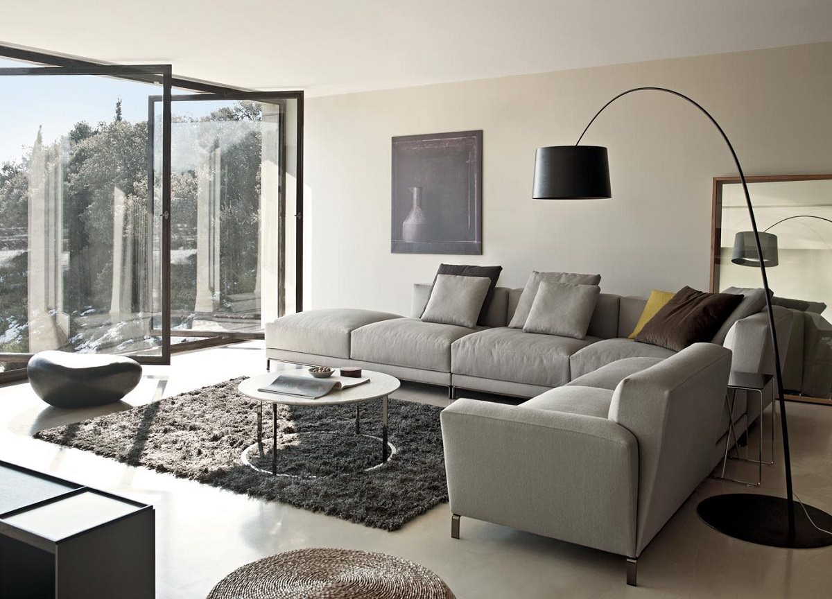  اتاق نشیمن مدرن که در طراحی آن از فرش ساده پشمی پرز بلند تیره و مبل های ال شکل طوسی استفاده شده است